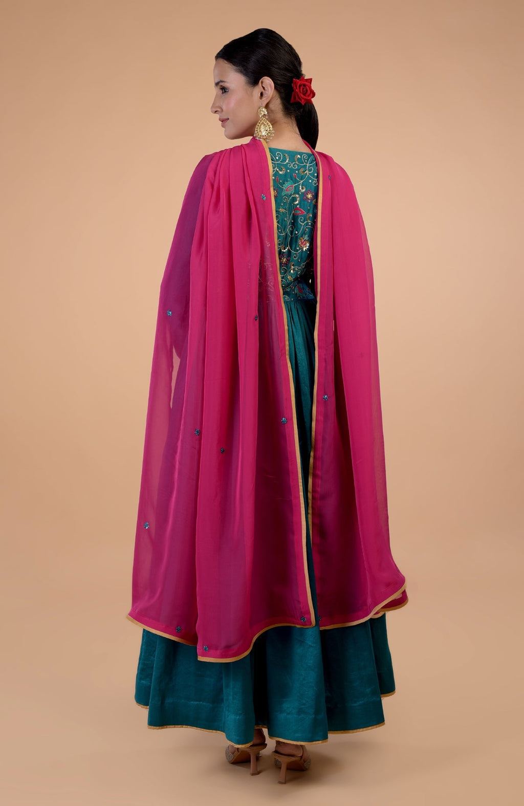 A woman models a teal anarkali set with a pink dupatta and gold embroidery.