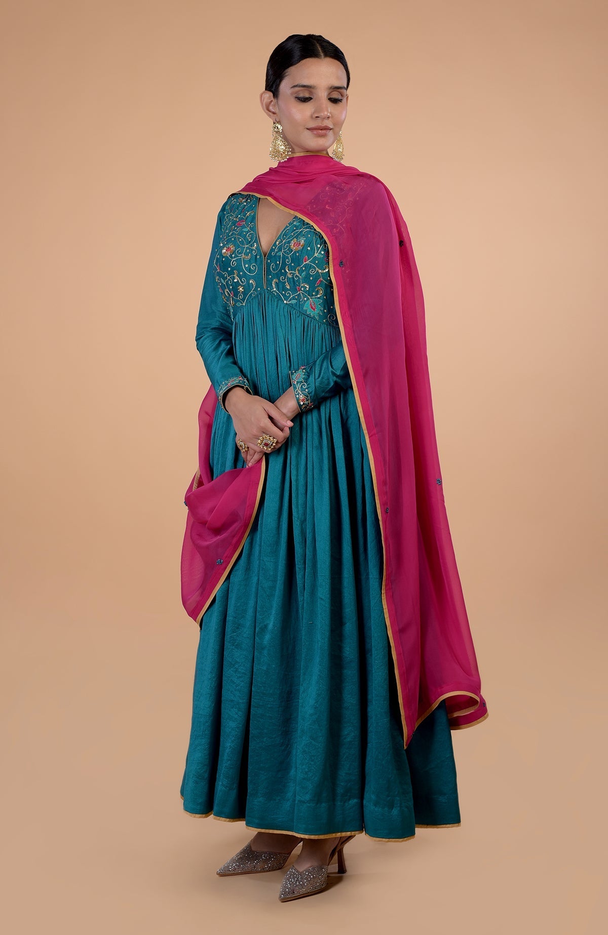 A woman models a teal anarkali with gold embroidery and a pink dupatta.