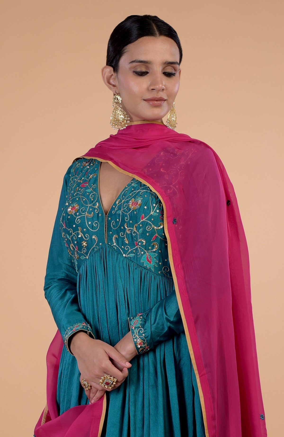A woman in a teal anarkali with pink dupatta and gold embroidery.