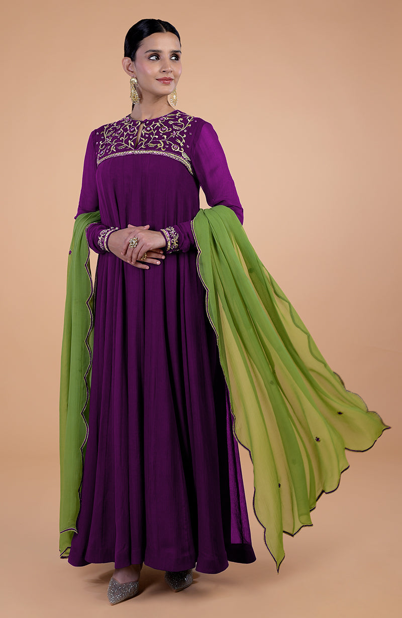 A woman models a plum anarkali set with green dupatta and gold embroidery.
