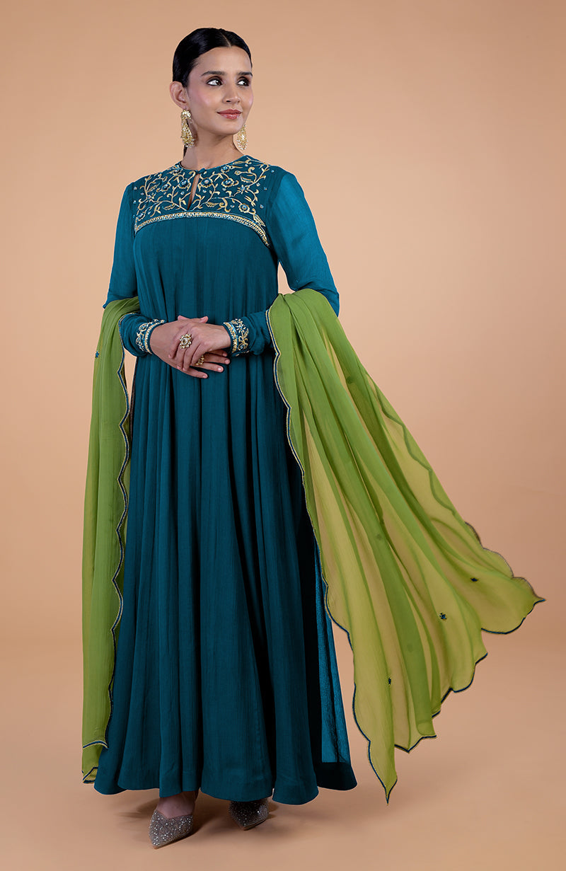 A woman models a teal-green anarkali set with gold embroidery and a green dupatta.
