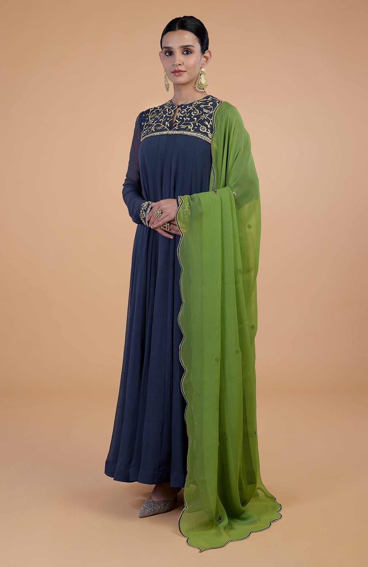 A woman models a plum anarkali set with green dupatta and gold embroidery.