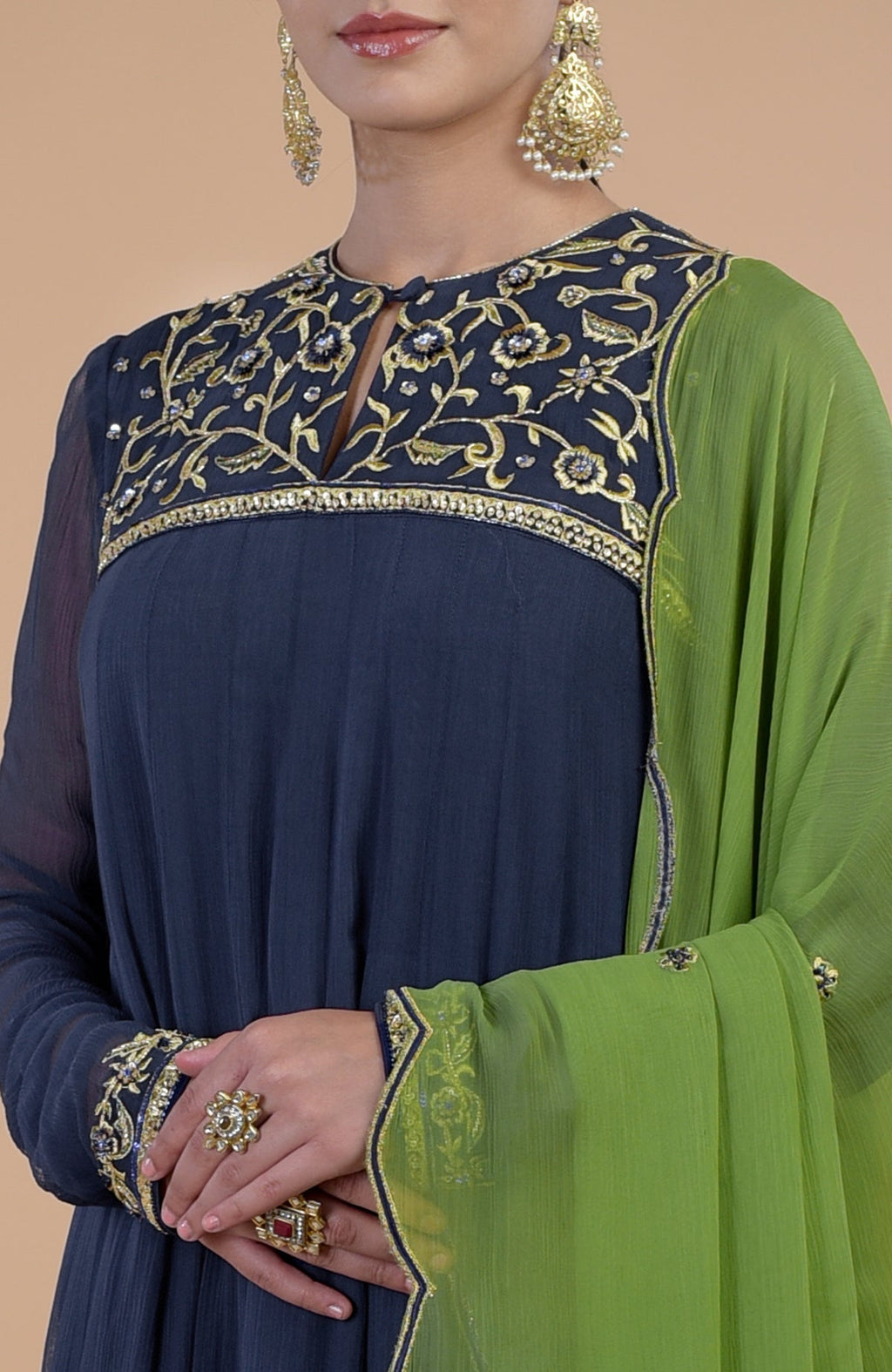 A woman models a midnight blue anarkali set with green dupatta and gold embroidery.