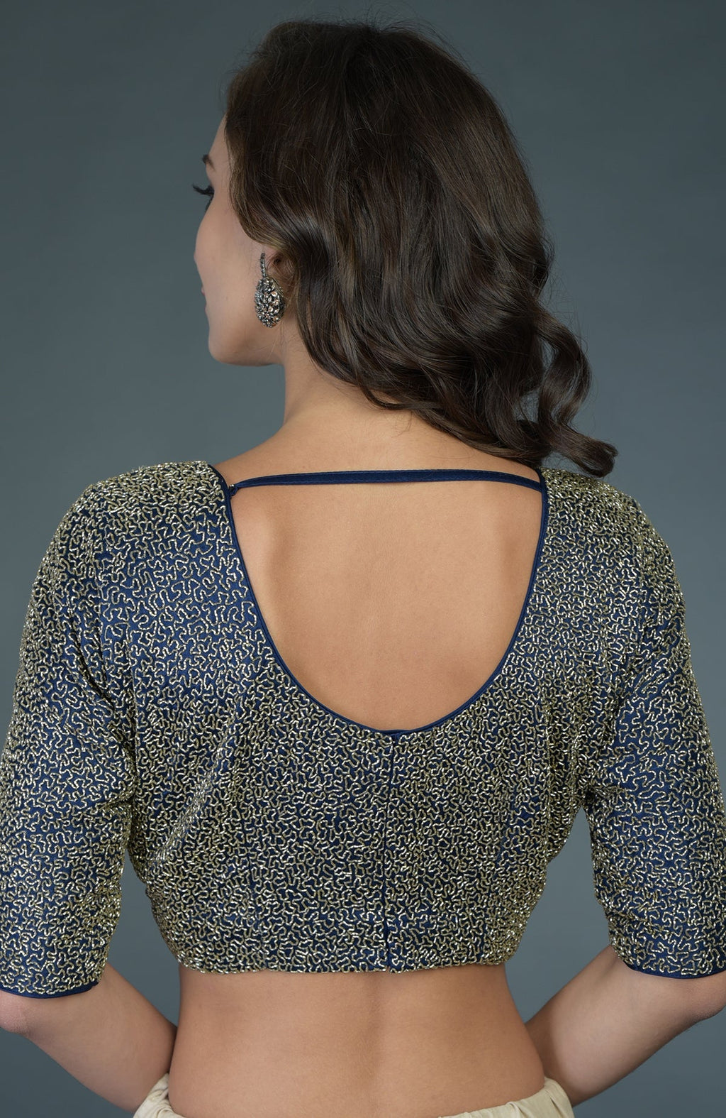 A woman models a bottle green zardozi work blouse with a deep U-shaped back.