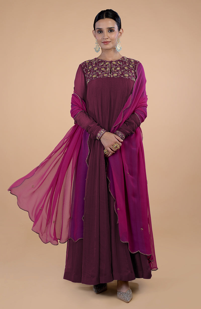 A woman models a teal-pink zardozi embroidered Anarkali set with a flowing dupatta.