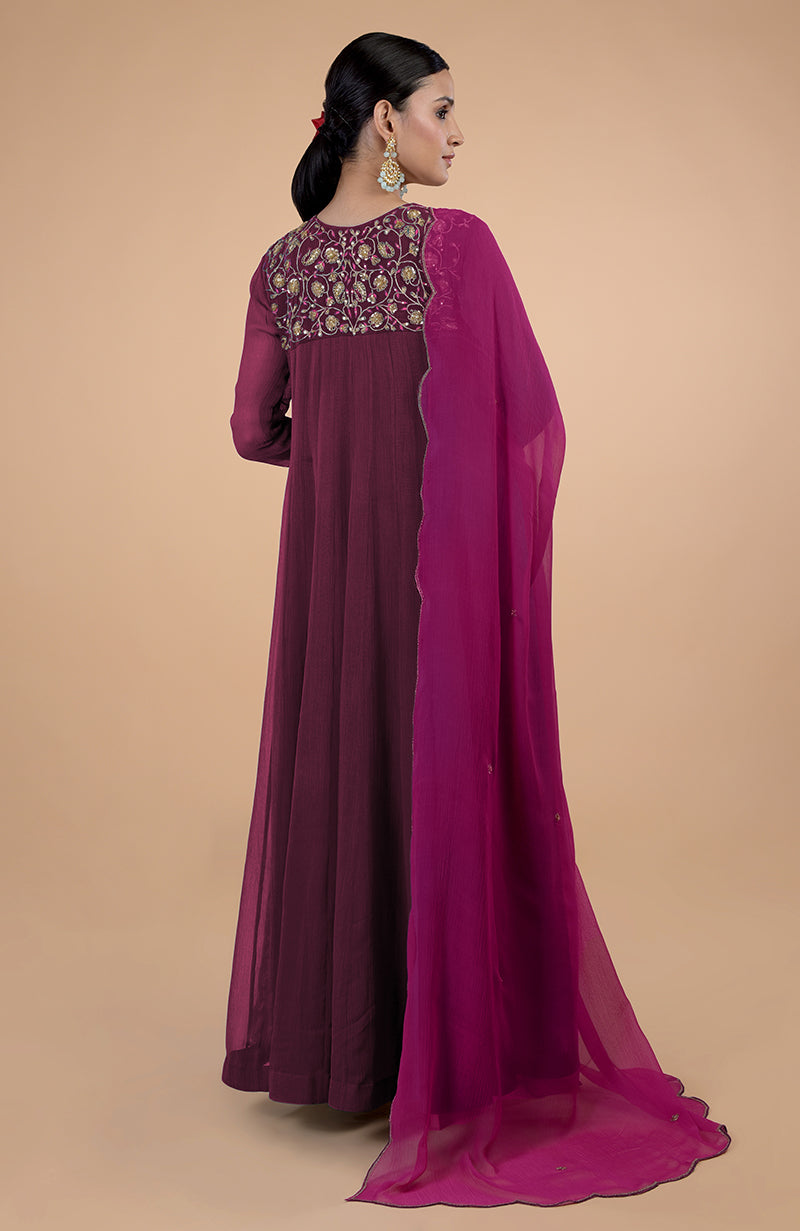 A woman models a burgundy anarkali with gold embroidery and a pink dupatta.