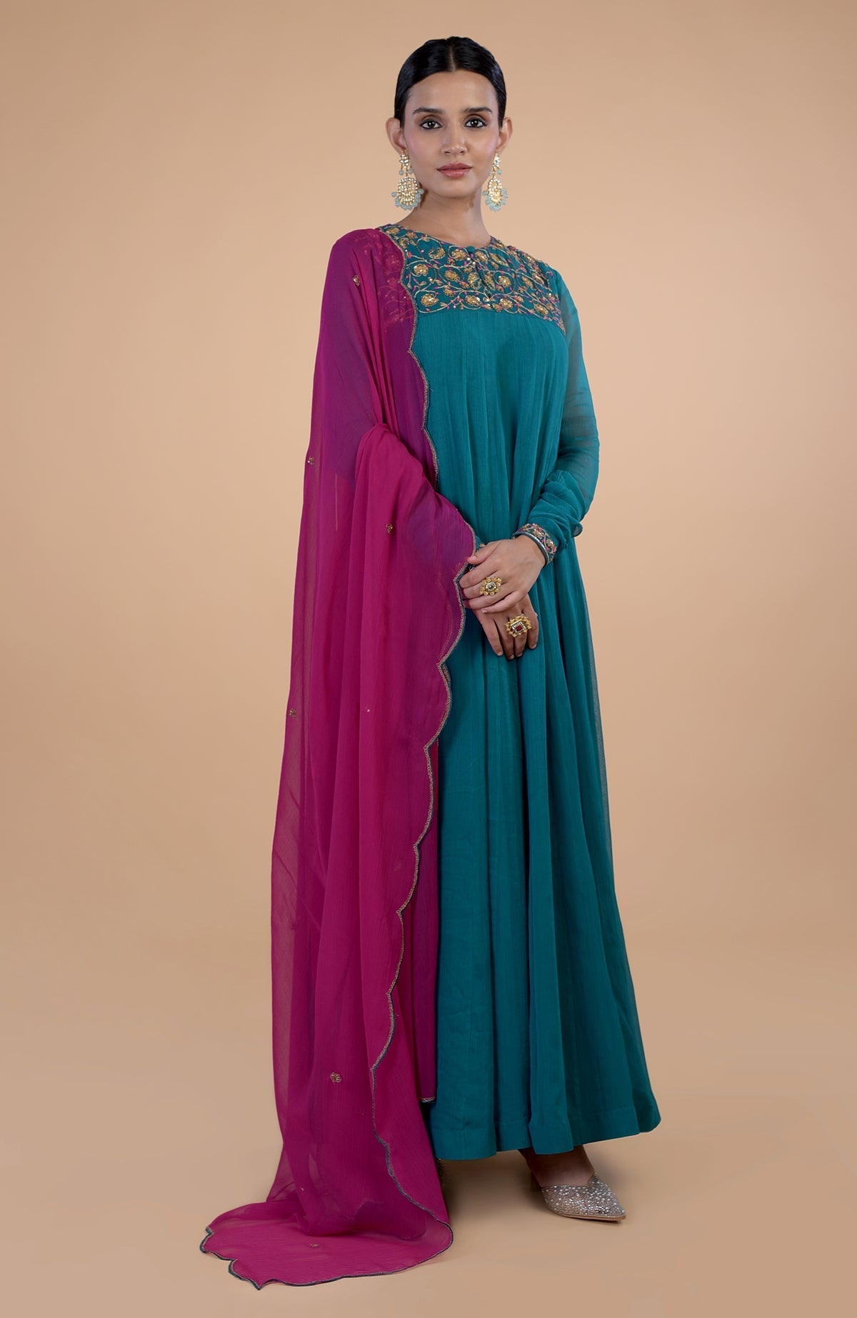 A woman models a teal anarkali with zardozi embroidery and a pink dupatta.