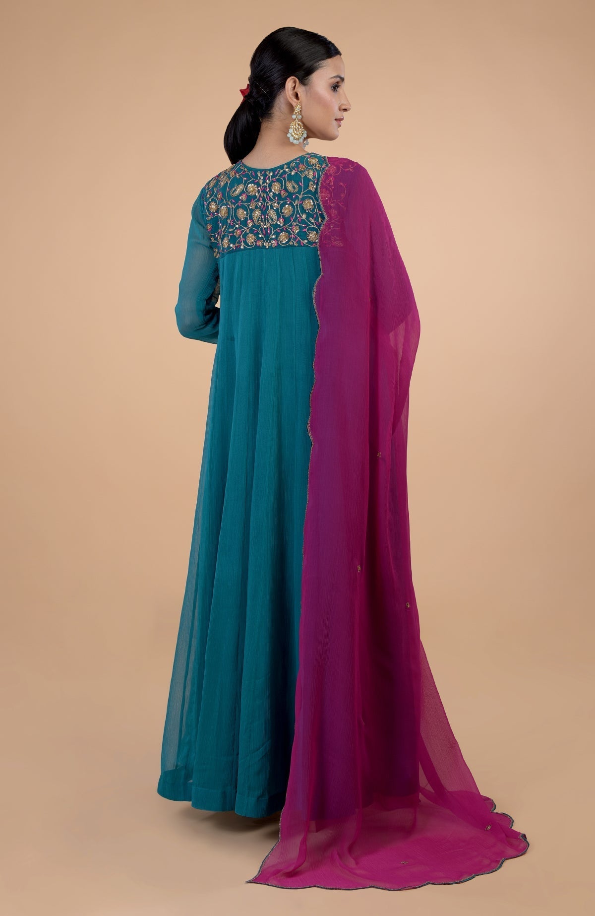 A woman models a teal anarkali with zardozi embroidery and a pink dupatta.