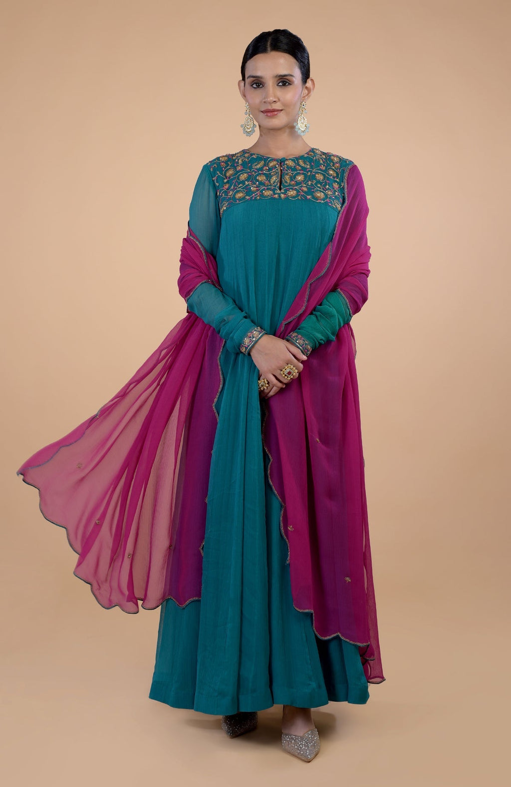 A woman models a teal and pink zardozi embroidered Anarkali set with a flowing dupatta.