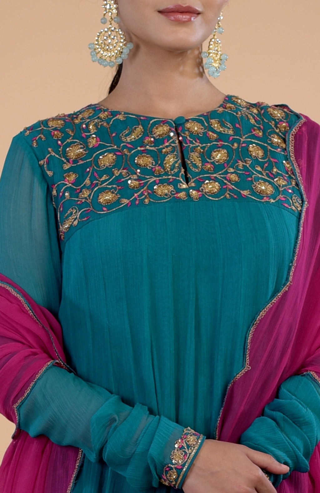 A woman wears a teal anarkali with gold and pink embroidery, paired with a pink dupatta.