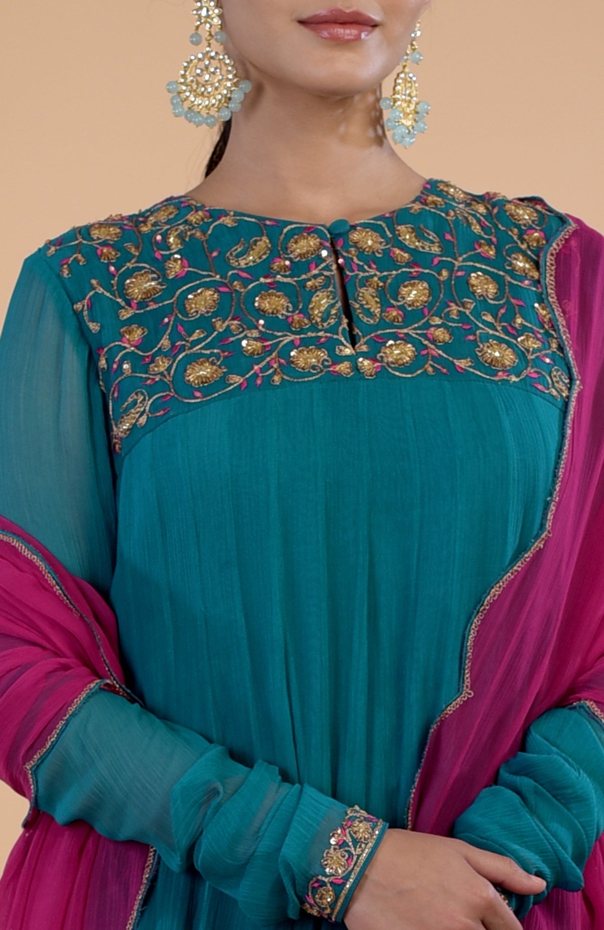 A woman wears a teal anarkali with gold and pink embroidery, paired with a pink dupatta.