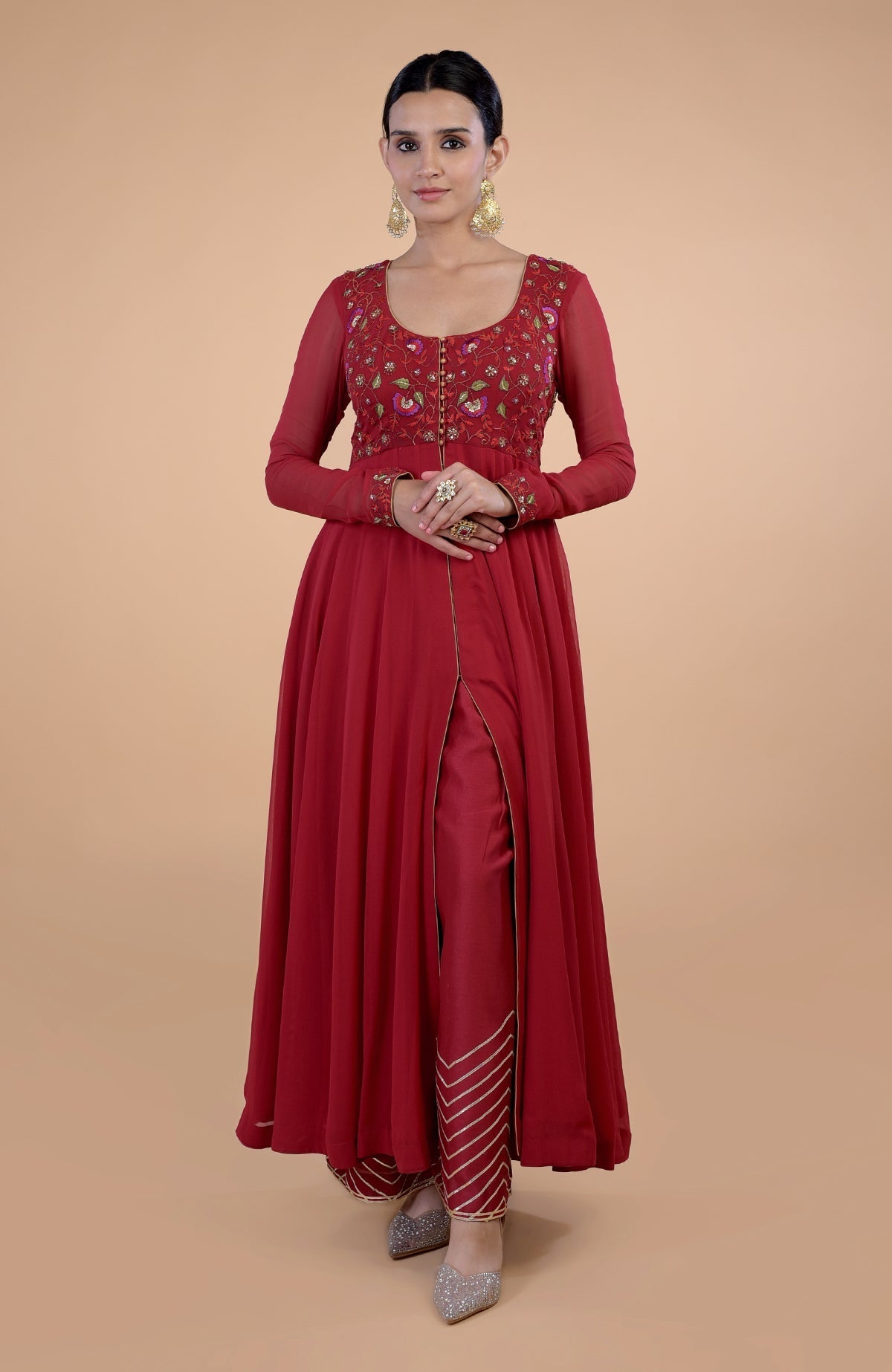 A woman models a blood red anarkali set with floral embroidery and gold accents.