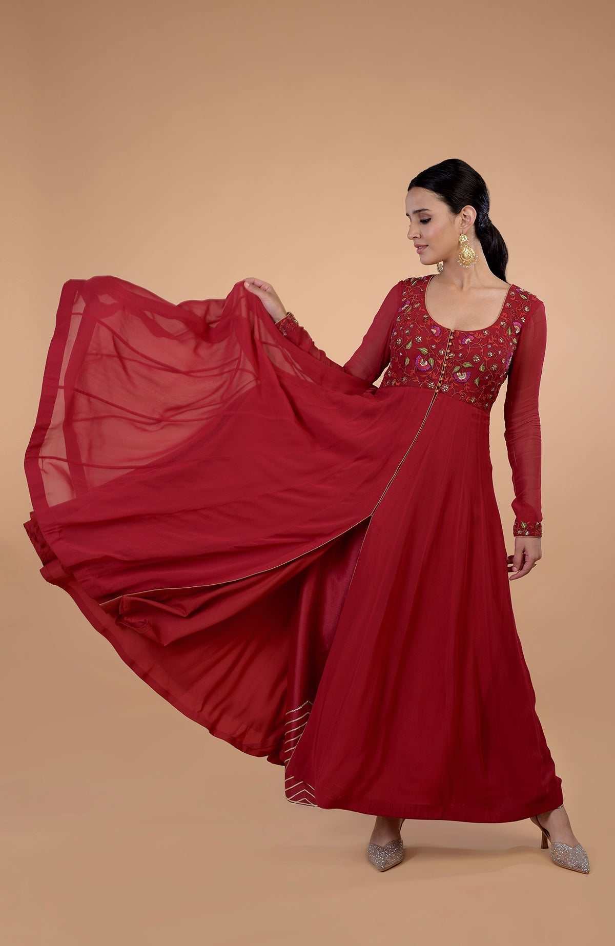 A woman in a blood red anarkali set with floral embroidery and a flowing skirt.