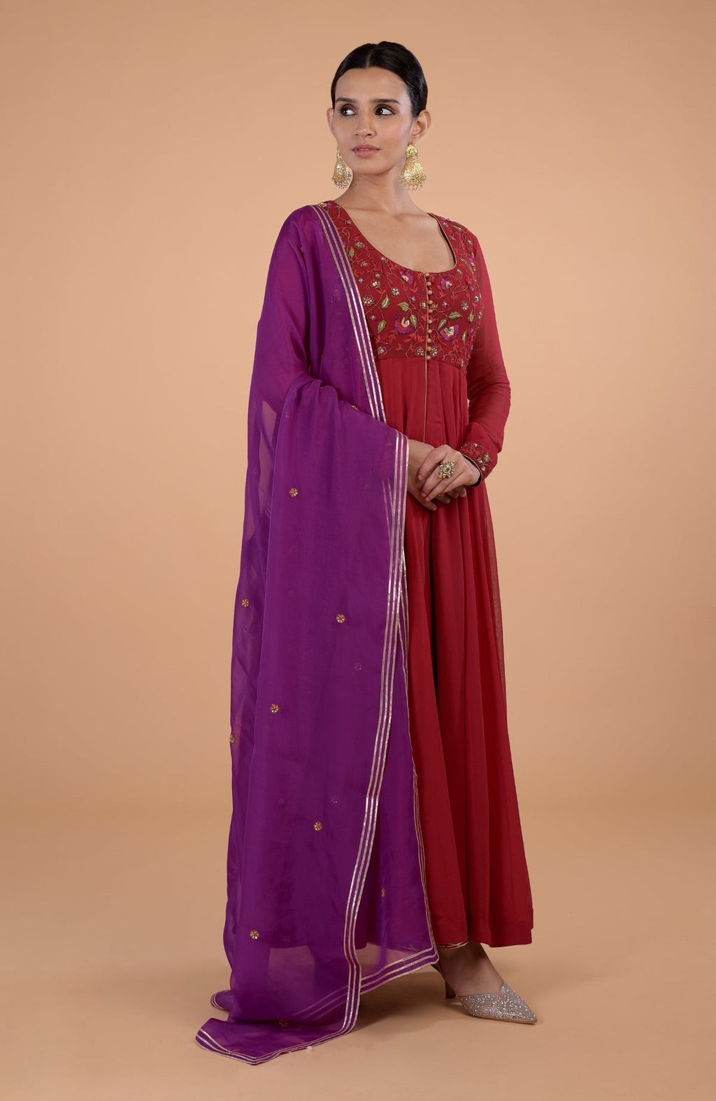 A woman models a blood red and purple Anarkali set with intricate embroidery.