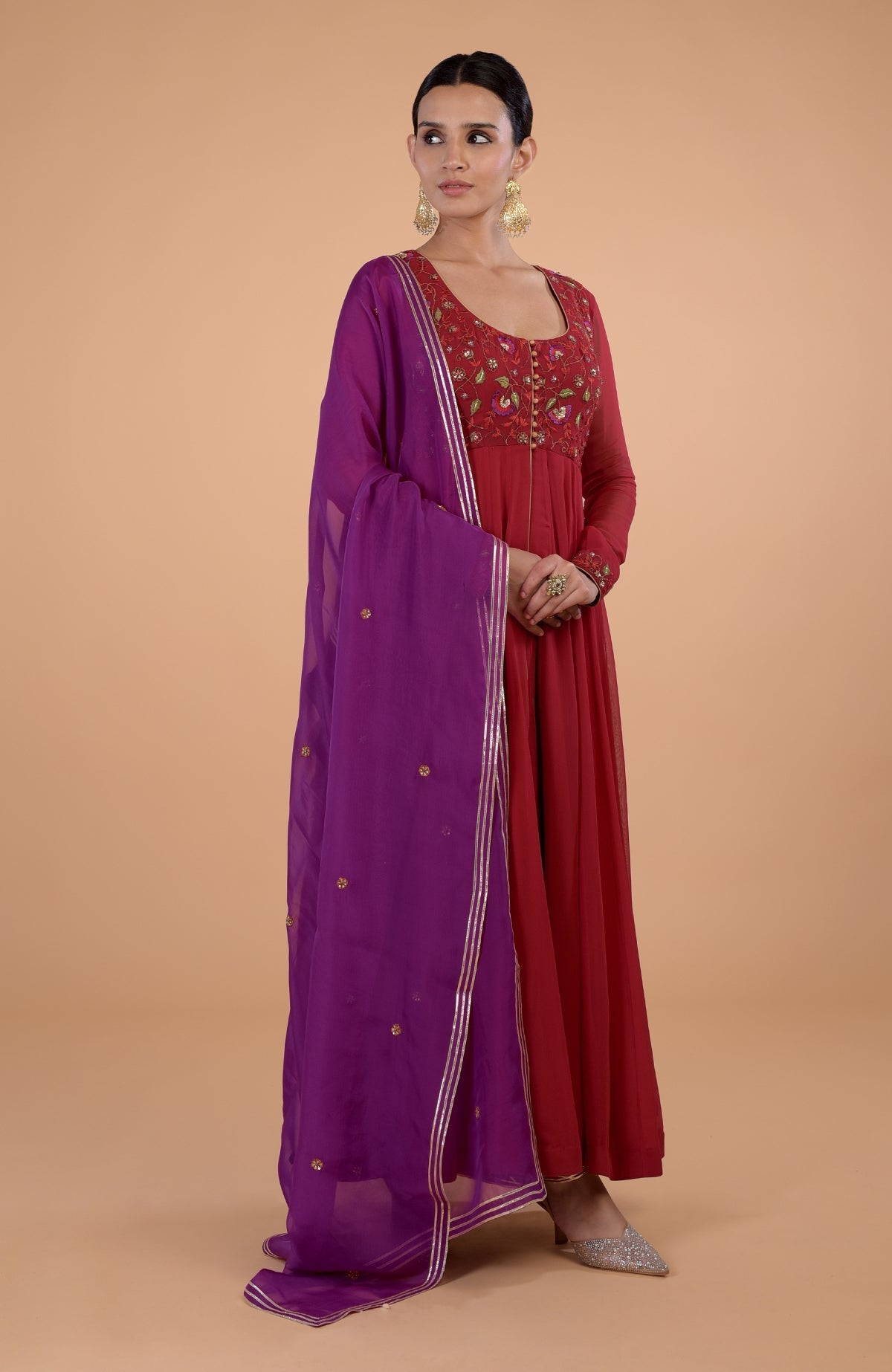 A woman models a blood red and purple Anarkali set with intricate embroidery.