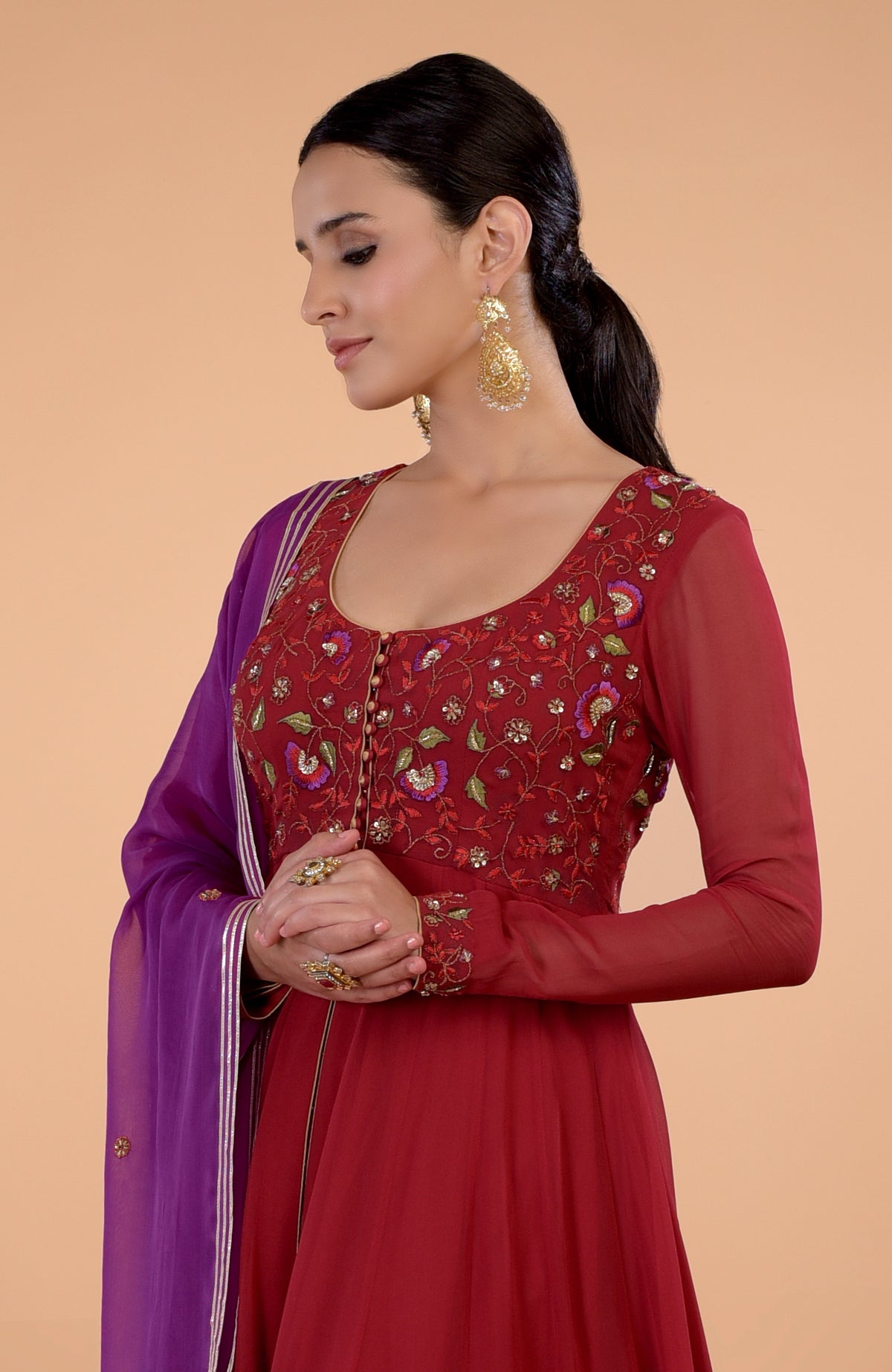 A woman models a blood red and purple anarkali set with intricate embroidery.