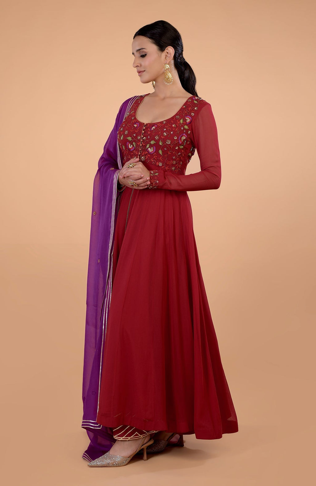 A woman models a blood red Anarkali set with a purple dupatta and embroidered bodice.