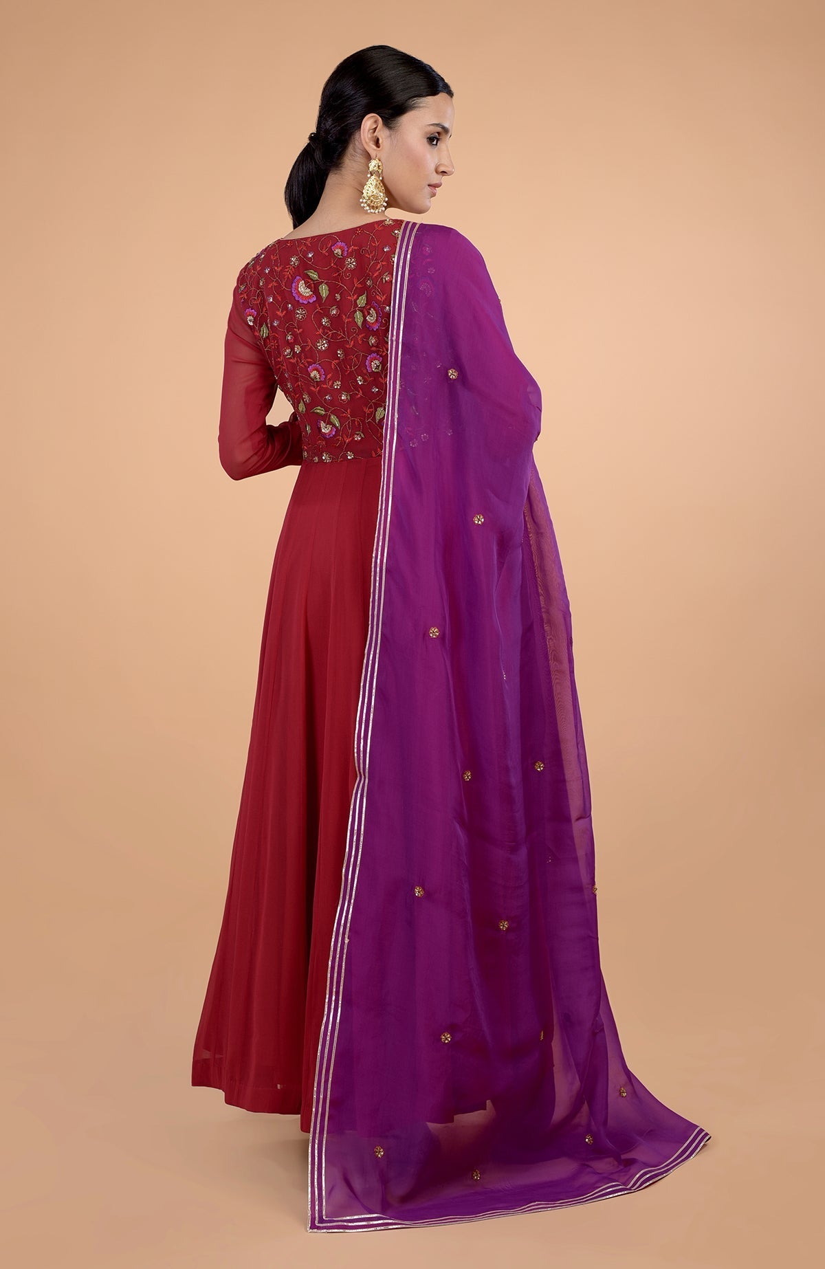 Woman in a blood red anarkali with embroidered bodice and purple dupatta.