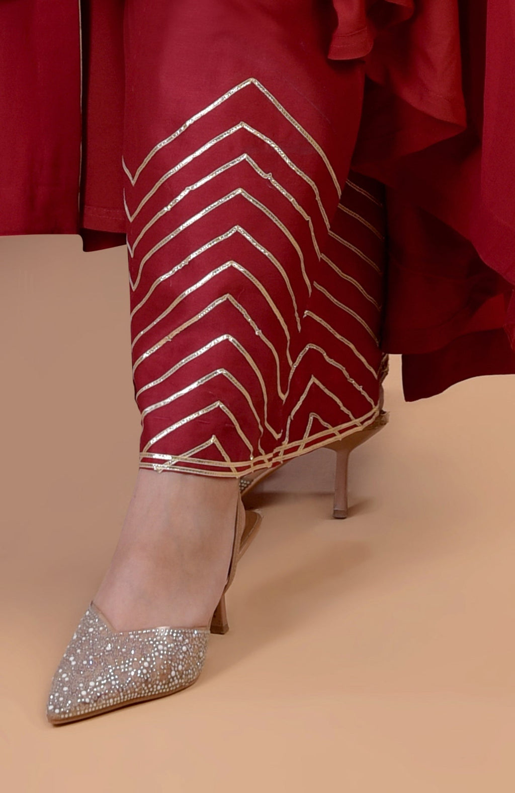A person wears a red garment with gold chevron patterns and sparkling pointed-toe heels.