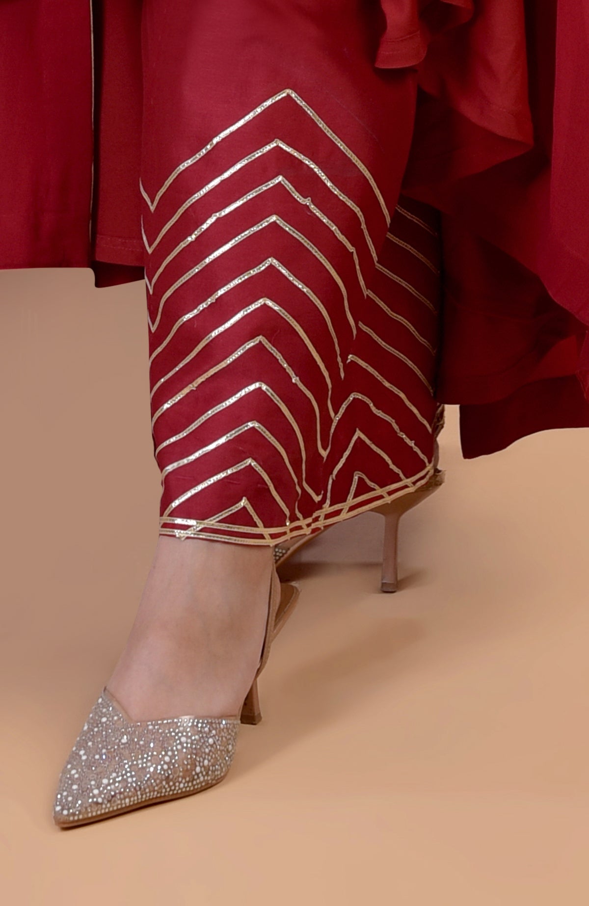 A person wears a red garment with gold chevron patterns and sparkling pointed-toe heels.
