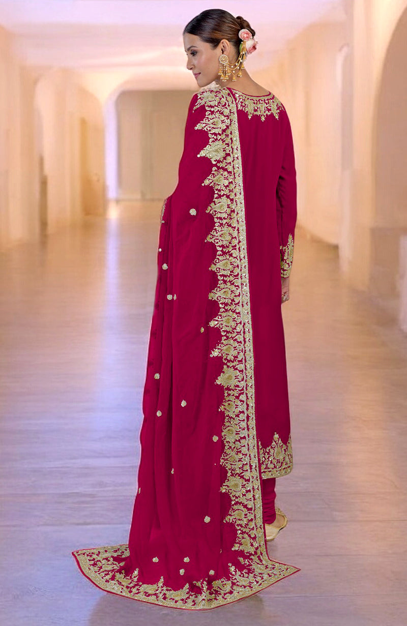 A woman in a bright rose gold embroidered kurta set stands in a hallway.