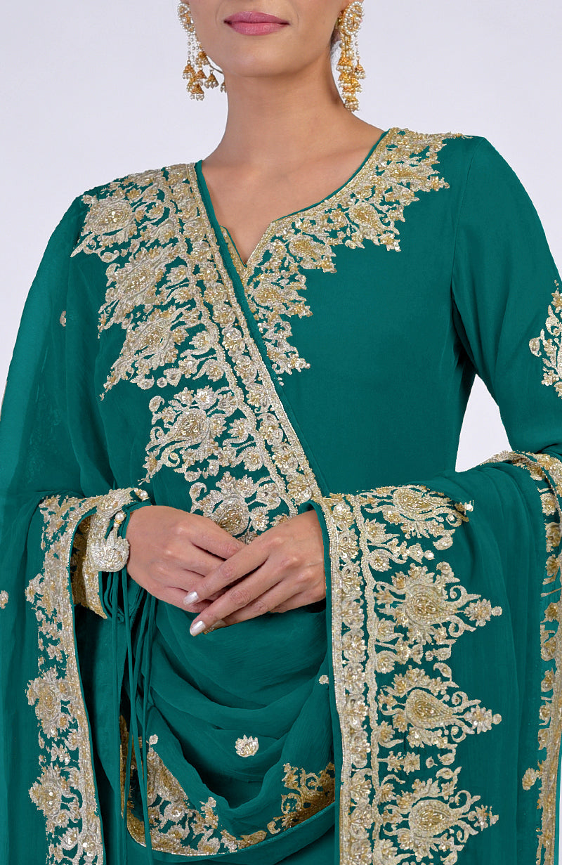 A woman models a teal kurta set with intricate gold embroidery and matching earrings.