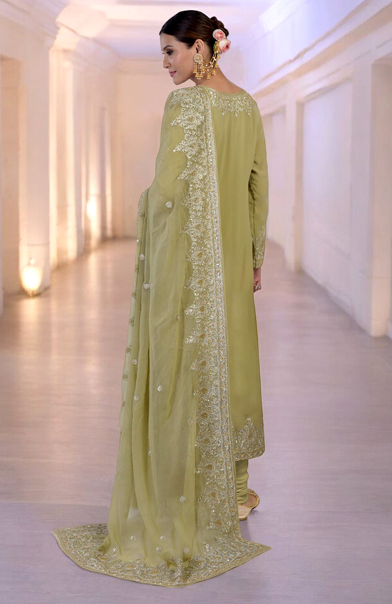 A woman in a bog green kurta set with gold embroidery stands in a hallway.