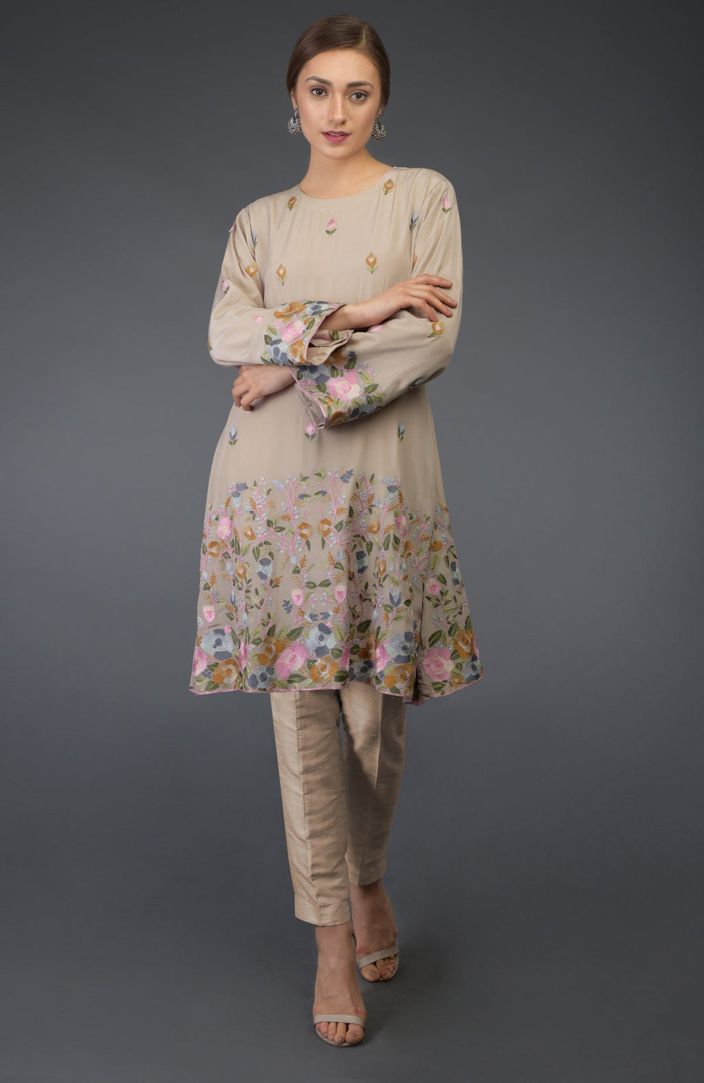 A woman models a beige Parsi embroidered tunic suit with floral patterns.