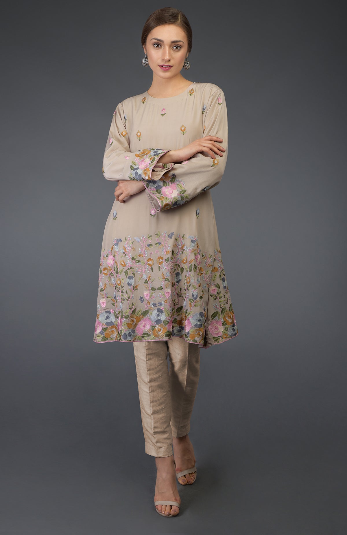 A woman models a beige Parsi embroidered tunic suit with floral patterns.