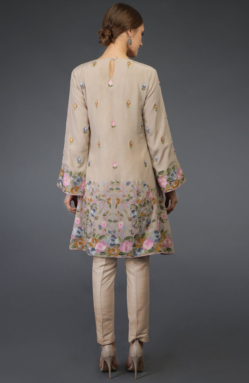 A woman models a beige Parsi embroidered tunic suit with floral patterns.