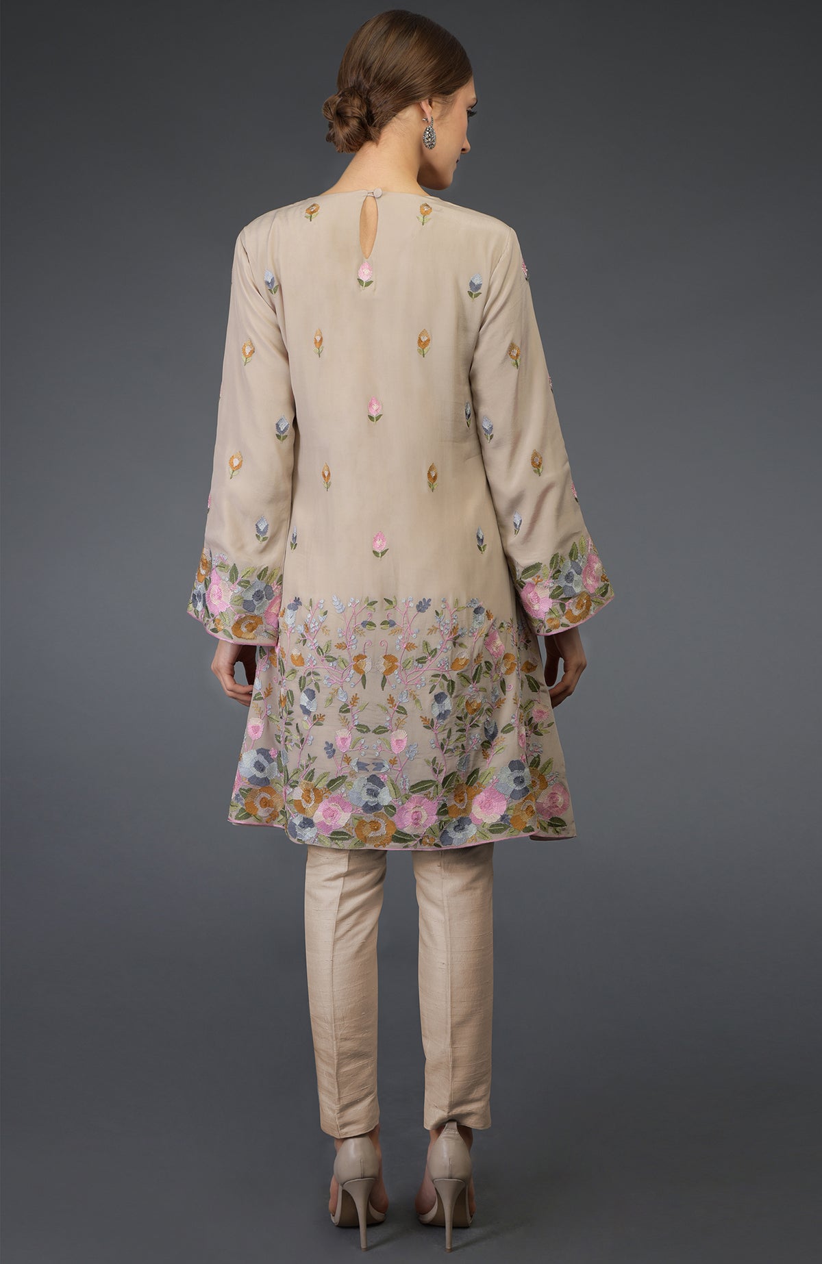 A woman models a beige Parsi embroidered tunic suit with floral patterns.