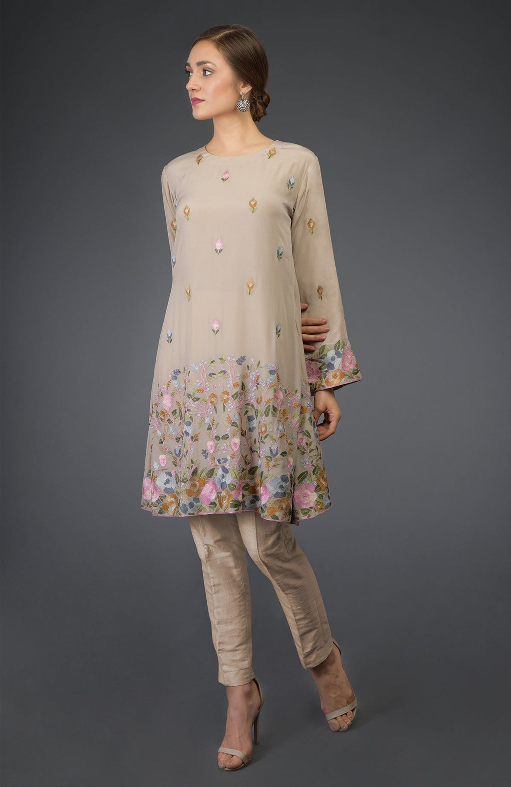 A woman models a beige Parsi embroidered tunic suit with floral patterns and matching pants.