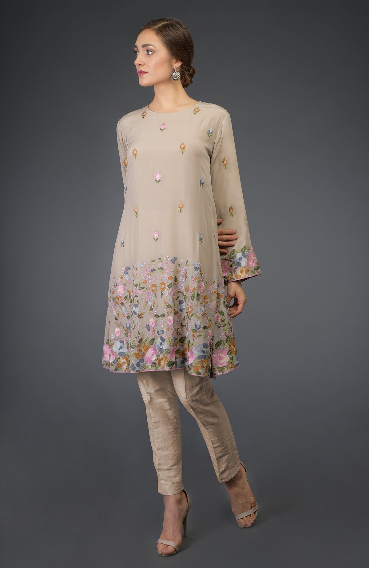 A woman models a beige Parsi embroidered tunic suit with floral patterns and matching pants.