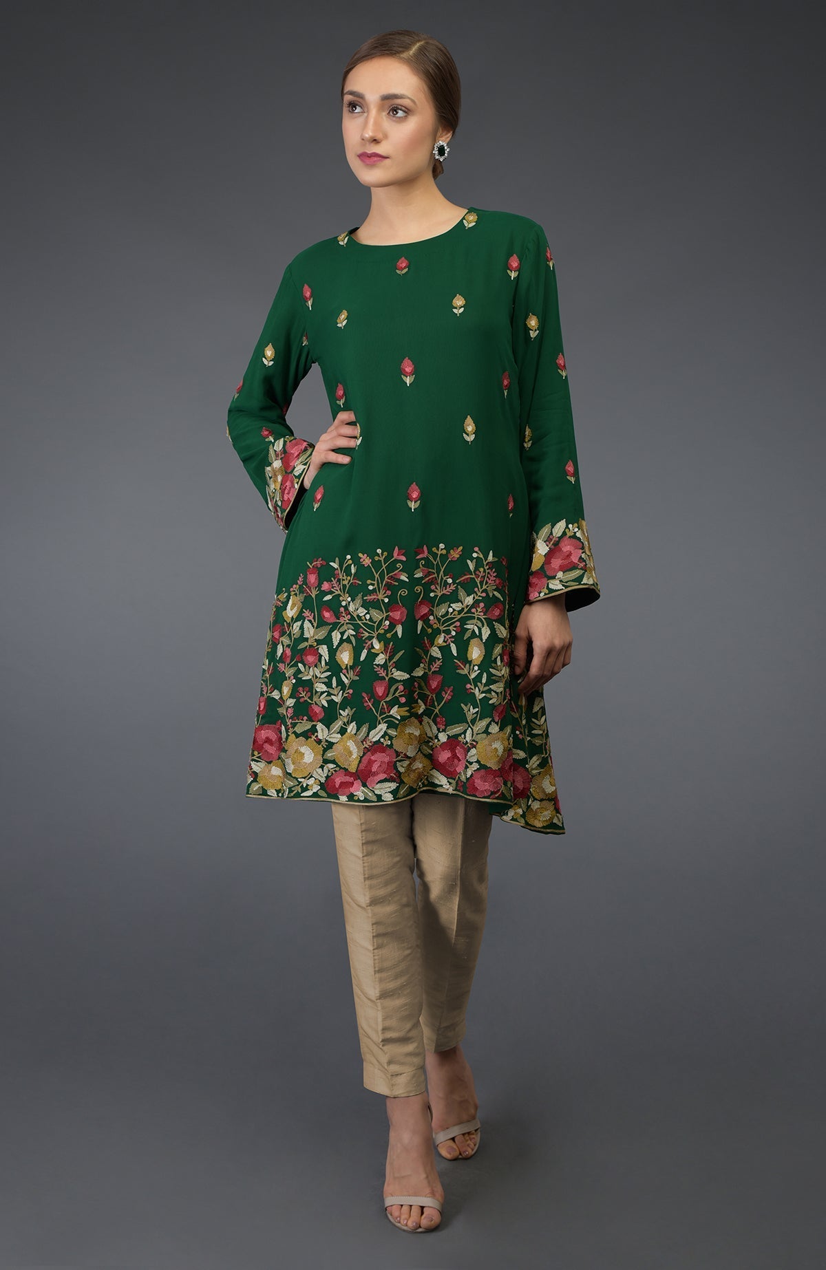 A woman models a bottle green Parsi embroidered tunic suit with beige pants.