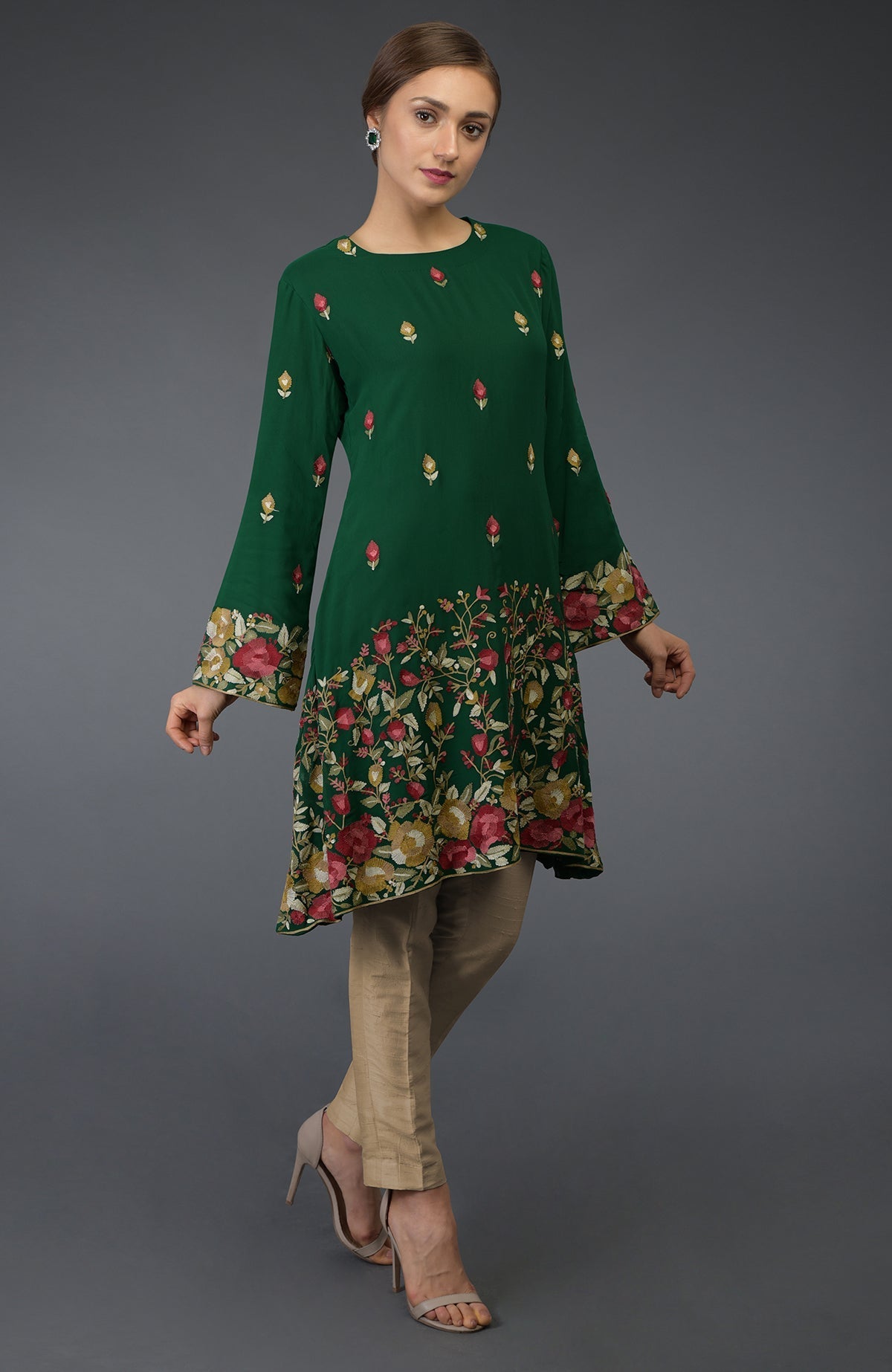 A woman models a bottle green Parsi embroidered tunic suit with beige pants.