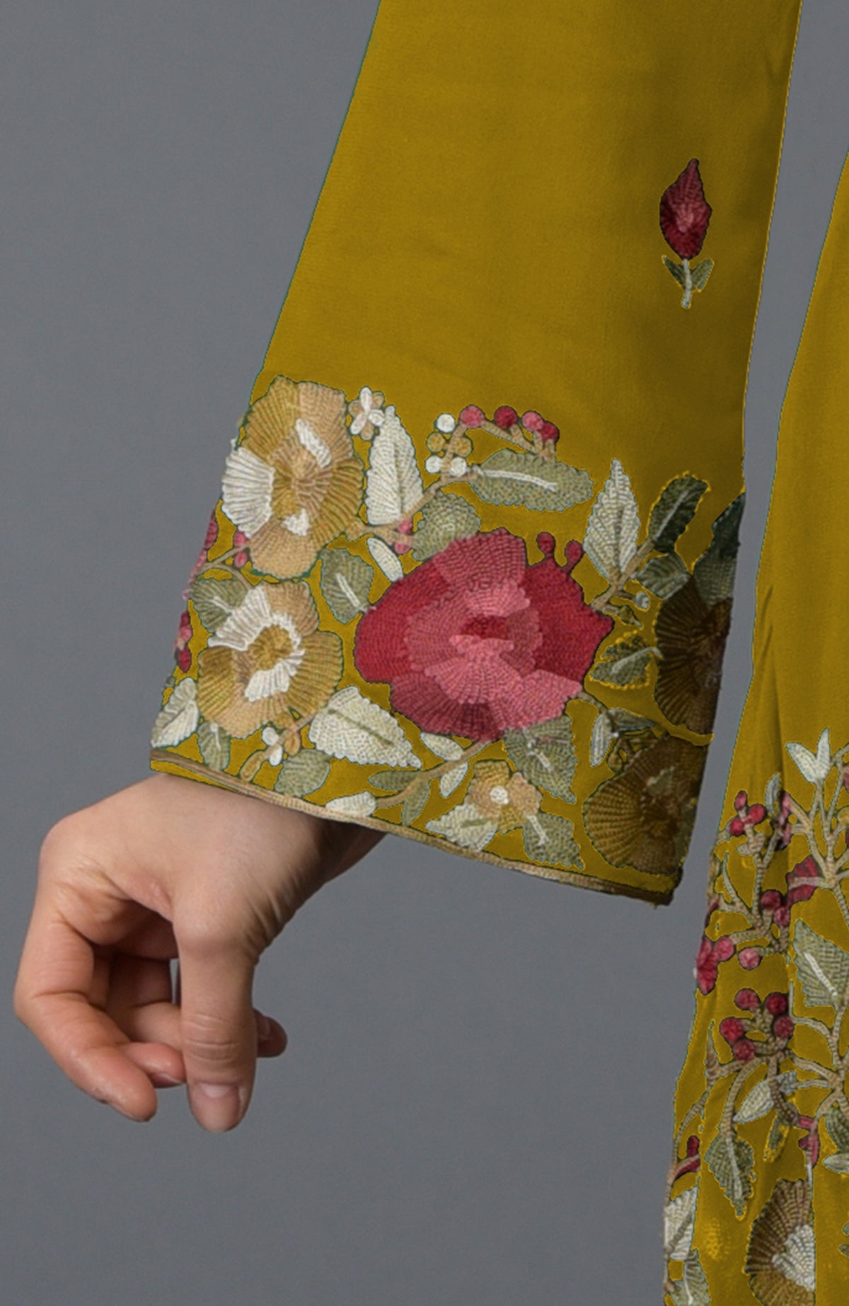 A woman's hand rests below a mustard tunic with Parsi floral embroidery.