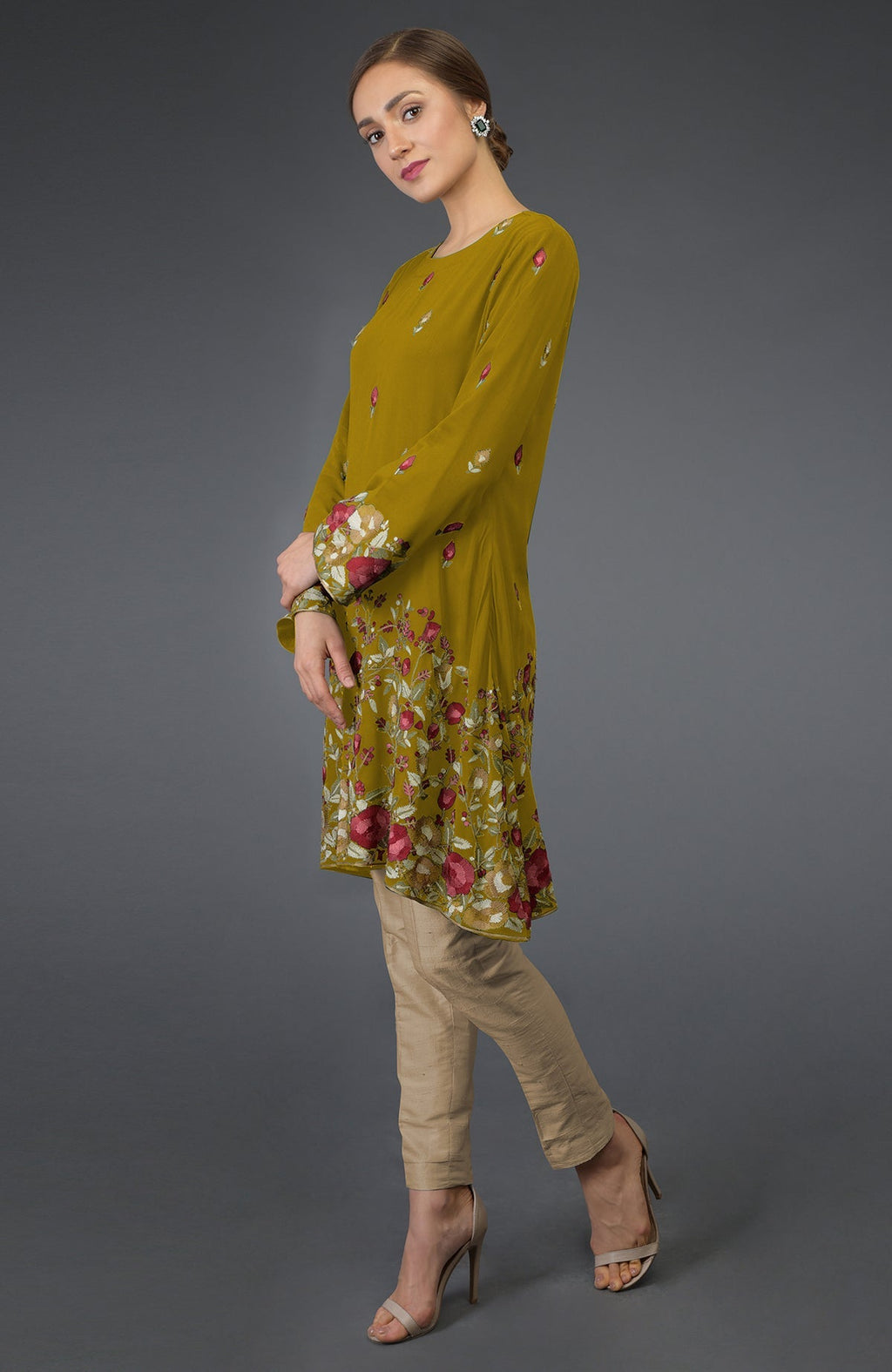 A woman models a mustard Parsi embroidered tunic suit with beige pants.