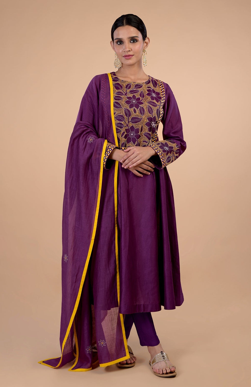 A woman models a plum kalidaar kurta set with Kantha embroidery and yellow piping.
