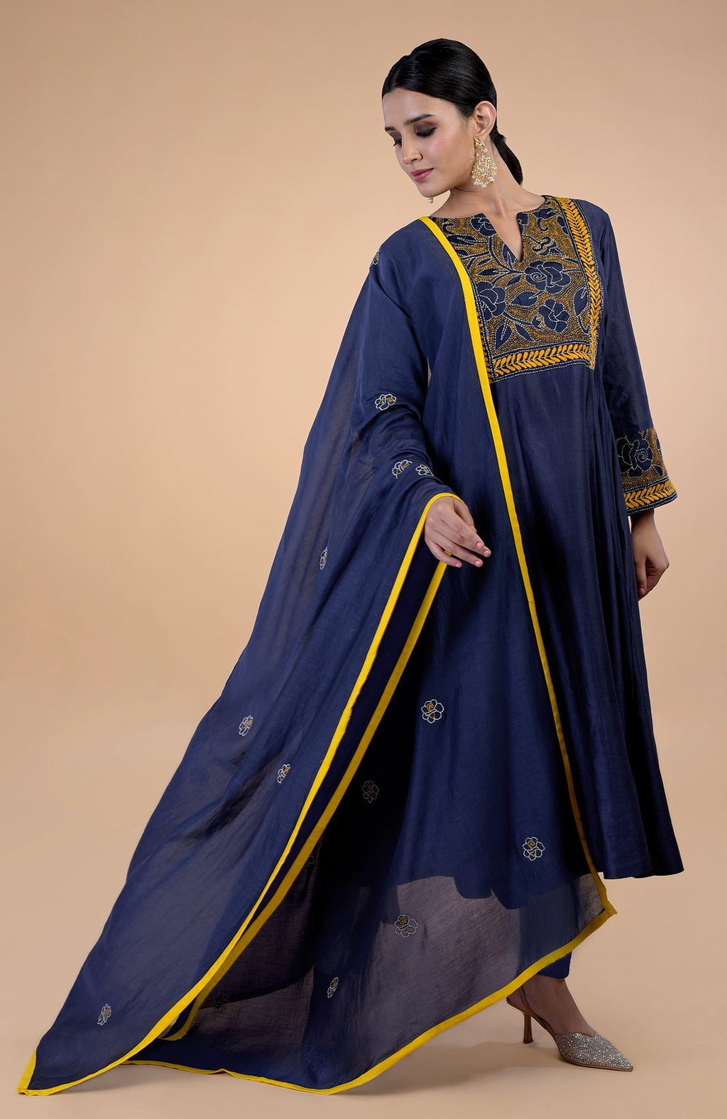 A woman models a navy blue Kantha hand-embroidered kalidaar kurta set with yellow trim.