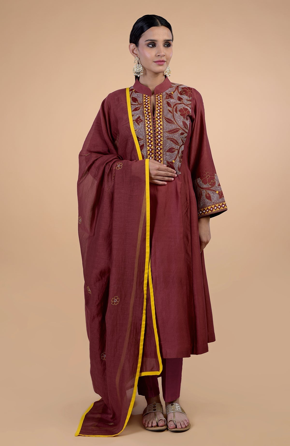 A woman models a rust Kantha hand-embroidered kalidaar kurta set with yellow piping.