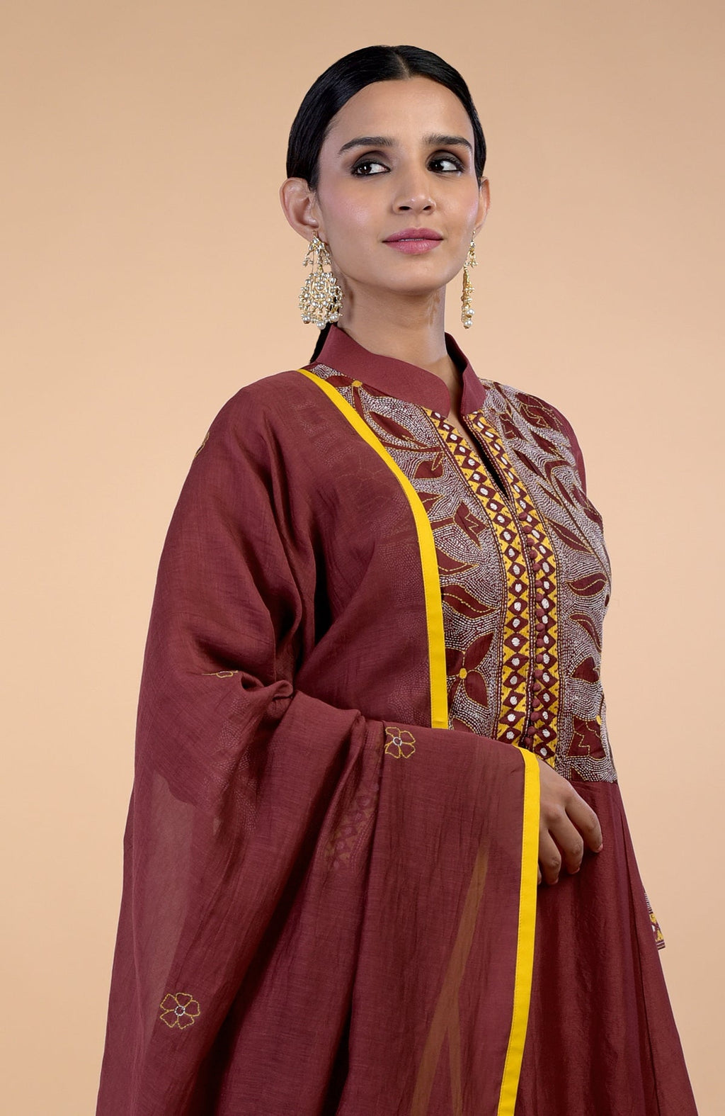 A woman models a rust kalidaar kurta set with Kantha embroidery and yellow piping.