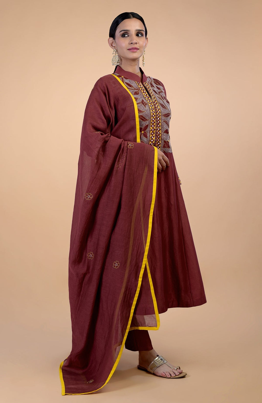 A woman models a rust Kantha hand-embroidered kalidaar kurta set with yellow piping.