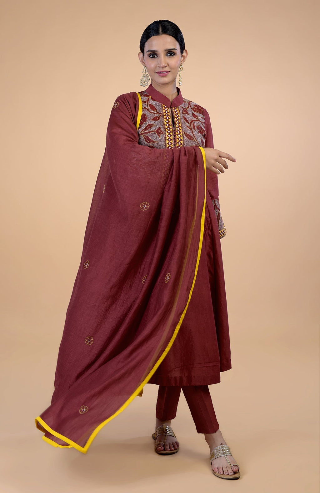 A woman models a rust Kantha hand-embroidered kalidaar kurta set with a yellow-piped dupatta.