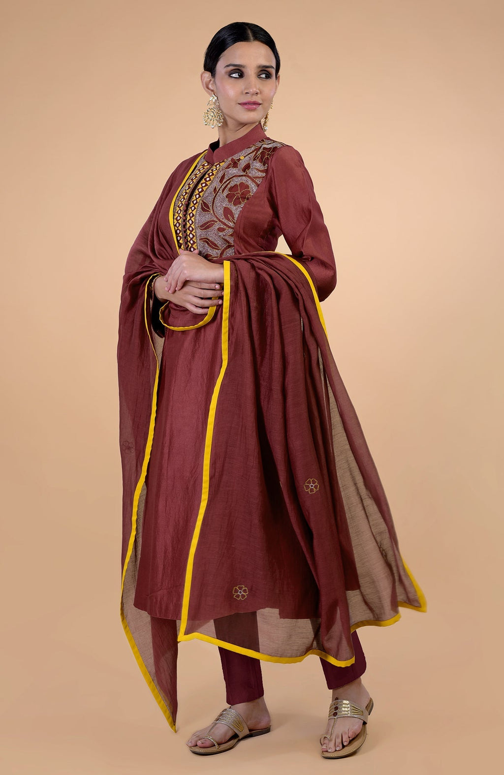 A woman models a rust-colored kurta set with Kantha embroidery and yellow piping.