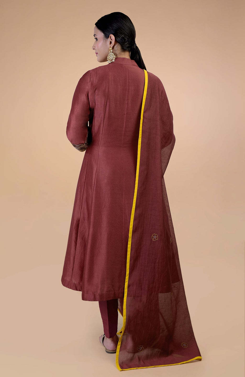 A woman from behind wears a rust kalidaar kurta set with a yellow-piped dupatta.