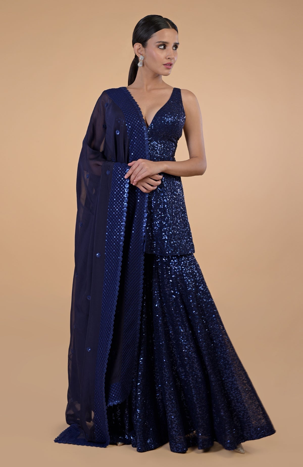 A woman models a sapphire blue sequin embroidered sharara set with a matching dupatta.