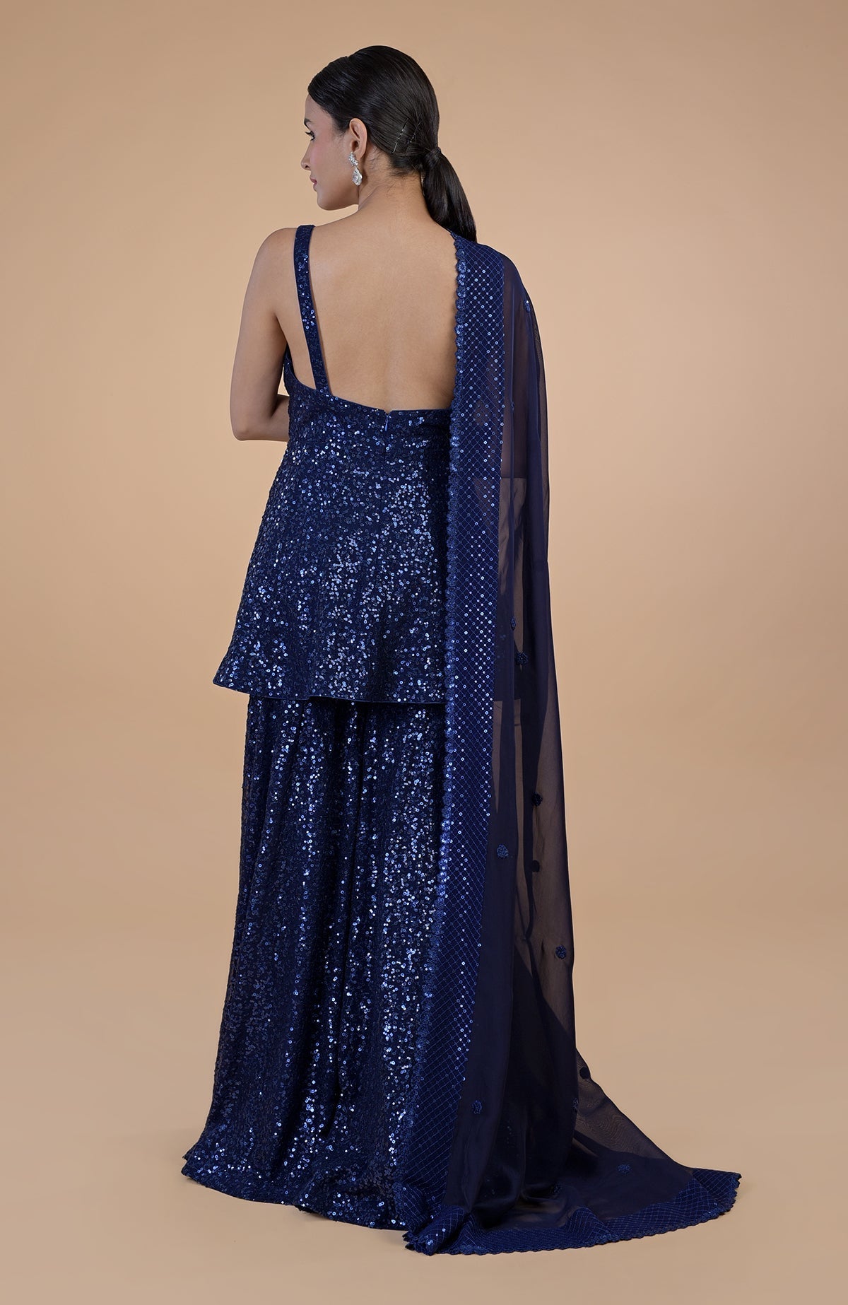 A woman models a sapphire blue sequin embroidered sharara set from the back.