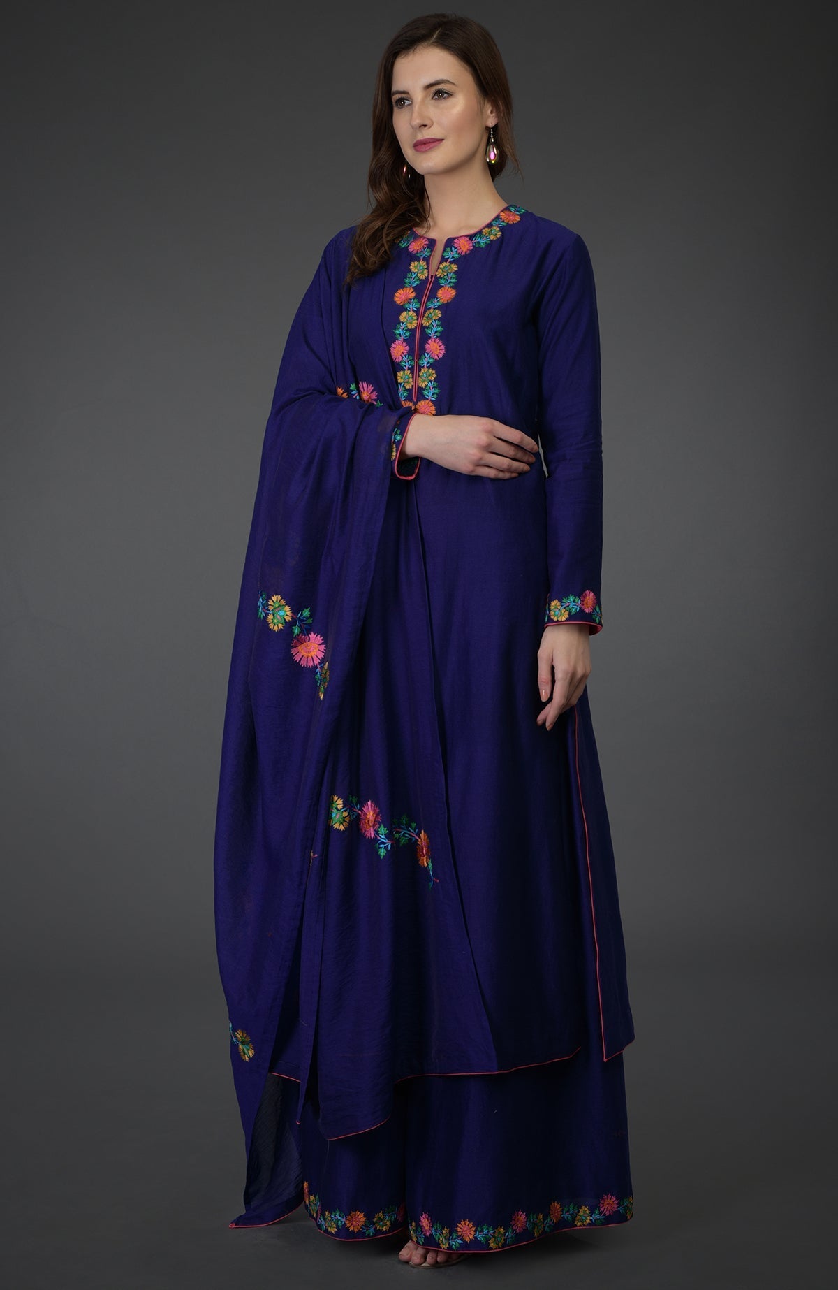 A woman models a blue palazzo suit with colorful floral embroidery.