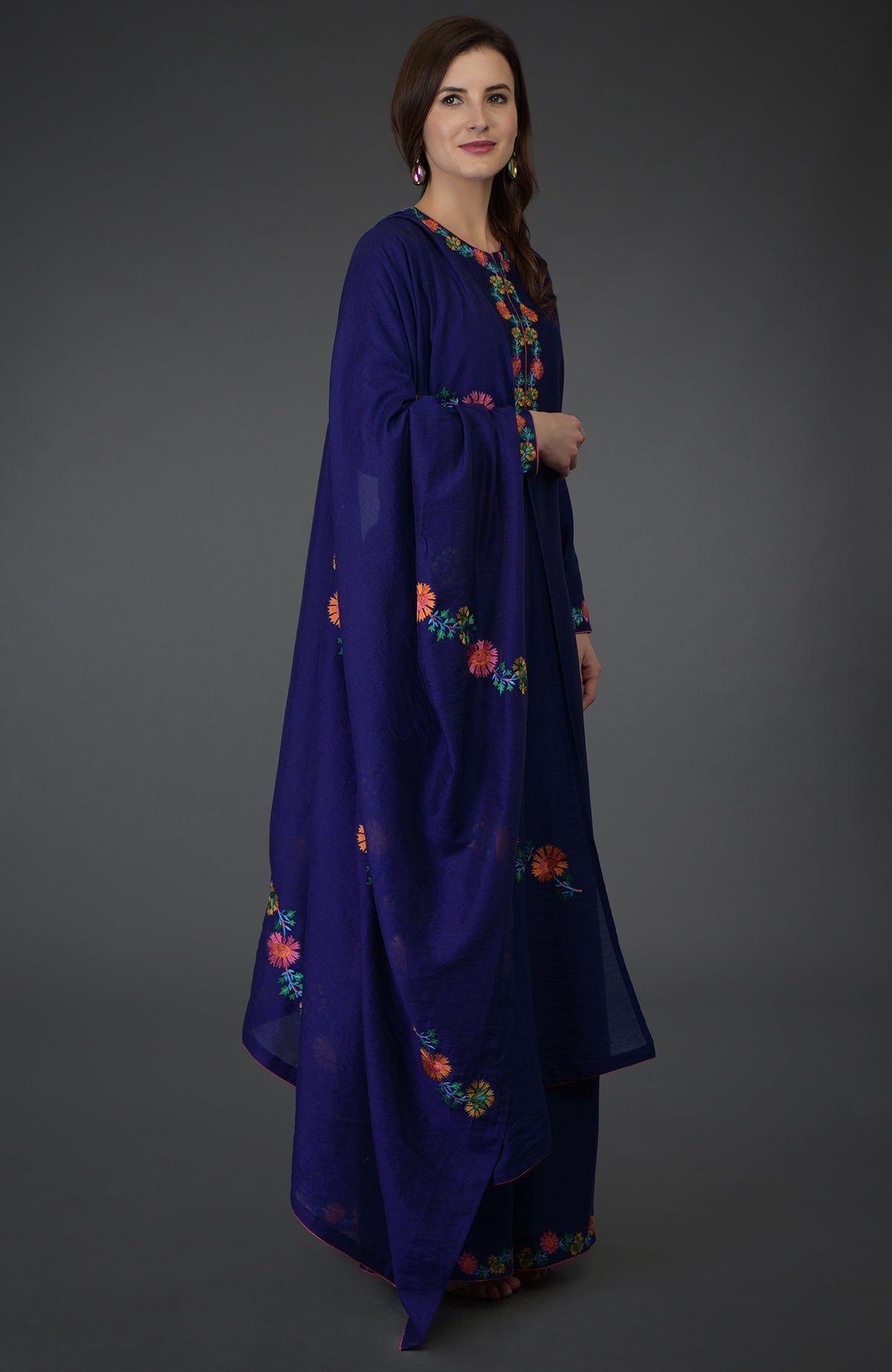 A woman models a blue palazzo suit with colorful floral embroidery.