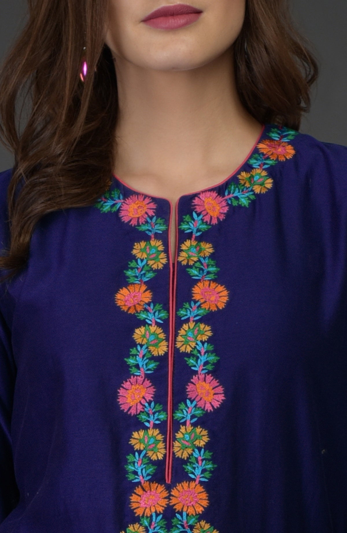 A woman wears a blue kurta with colorful floral embroidery along the neckline.